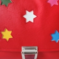 Ein Kindertraum wird wahr! Kindergartentasche aus hochwertigem, strapazierfähigem rotem Kunstleder mit bunten hinterlegten Sternen. Die Tasche hat einen reflektierenden Druckverschluss für eine gute Sichtbarkeit in der Dämmerung und einen verstellbaren Schulterträger für einen perfekten, bequemen Sitz . Ausgekleidet ist das Bijoux mit einem dekorativem Baumwollstoff. Jede Tasche ist in der Schweiz handgefertigt. Die Grösse von 23x18x7.5cm bietet Platz für eine Znünibox und eine kleine Trinkflasche 2dl